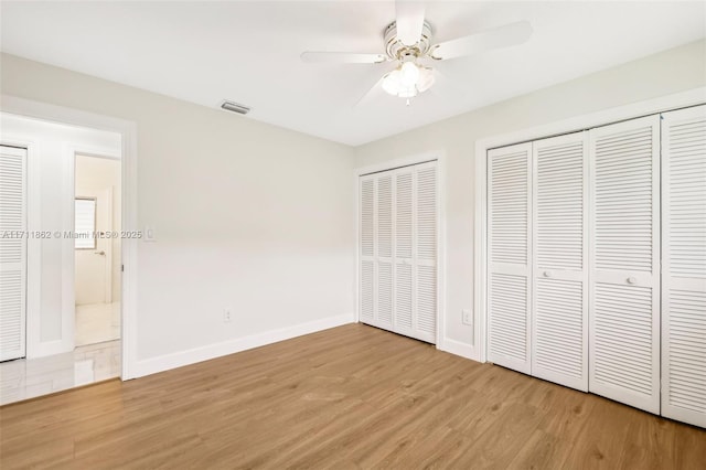 unfurnished bedroom featuring ceiling fan, wood-type flooring, and two closets