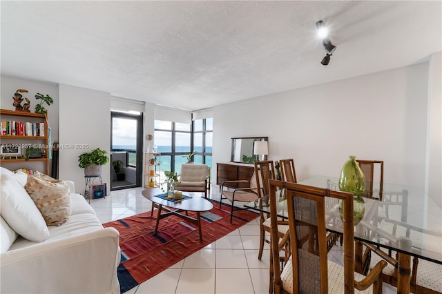 living room featuring expansive windows, a water view, a textured ceiling, and light tile patterned flooring