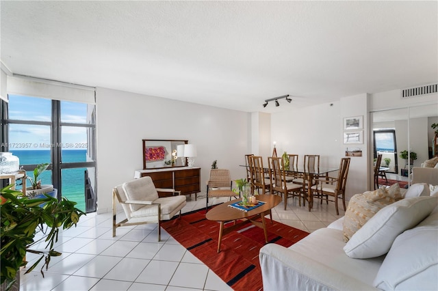 living room featuring a textured ceiling, a water view, light tile patterned floors, and rail lighting