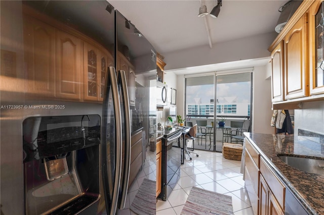 kitchen featuring appliances with stainless steel finishes, expansive windows, sink, light tile patterned floors, and dark stone countertops