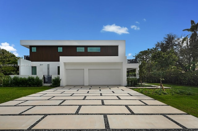 contemporary home featuring decorative driveway, a balcony, a front lawn, and stucco siding