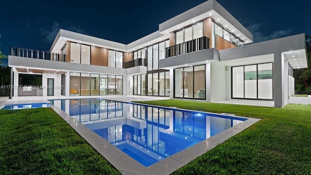 back of house at night featuring an outdoor pool, a patio area, a yard, and stucco siding