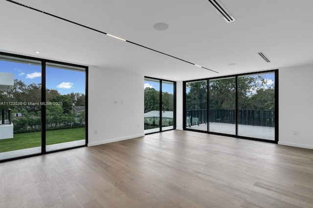 empty room with visible vents, baseboards, a wall of windows, and wood finished floors