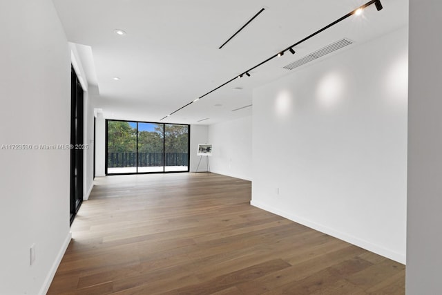 empty room featuring baseboards, expansive windows, visible vents, and wood finished floors