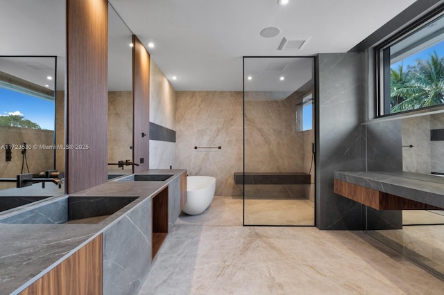 full bath with marble finish floor, walk in shower, vanity, a freestanding tub, and tile walls