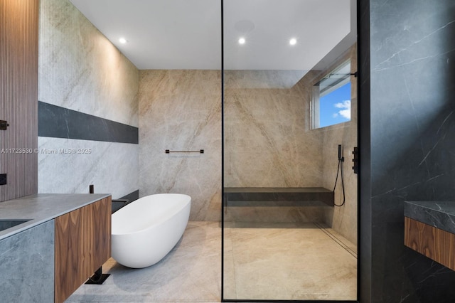 bathroom with a walk in shower, recessed lighting, vanity, tile walls, and a freestanding bath