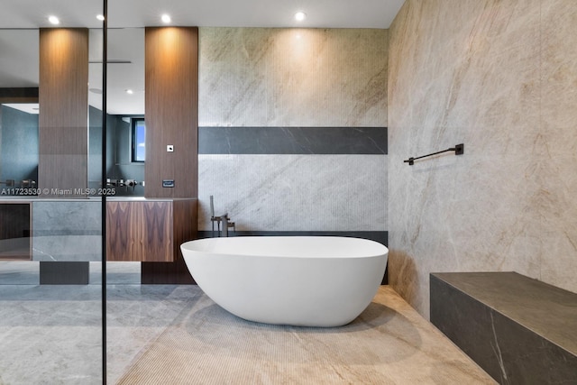 full bath featuring a freestanding tub, recessed lighting, tile walls, and vanity