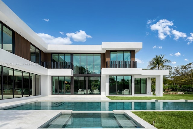 rear view of property with a pool with connected hot tub, a patio area, and a balcony