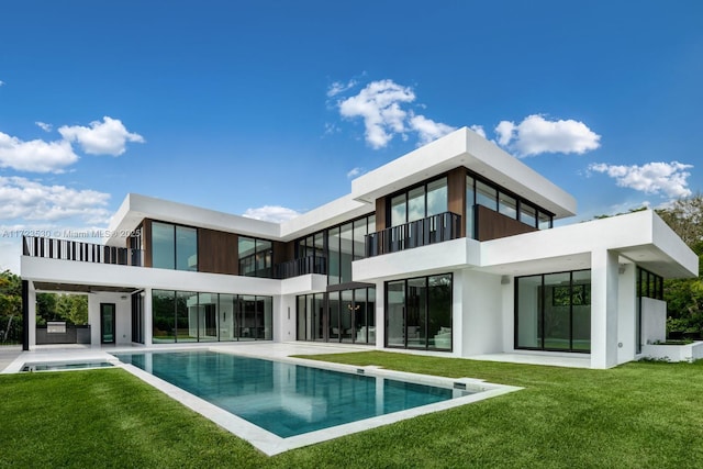 back of house featuring a balcony, an outdoor pool, a patio, and a yard