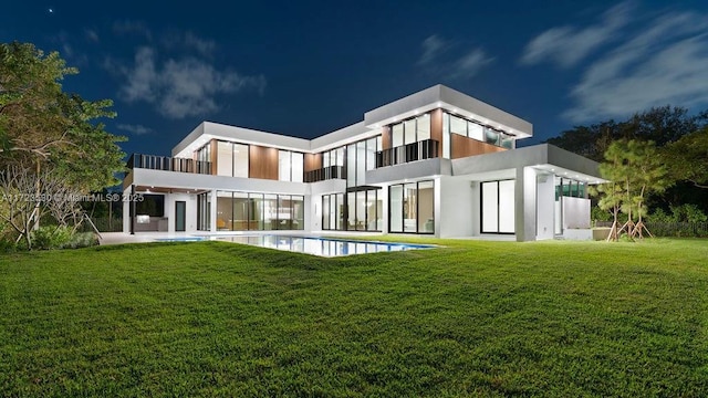 back of house at night featuring a lawn, an outdoor pool, and stucco siding