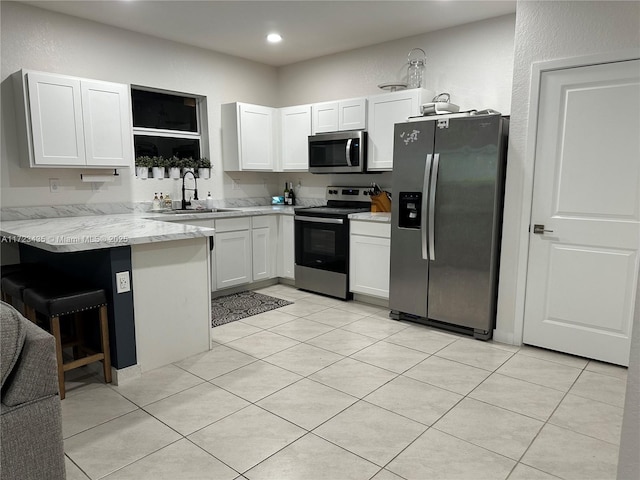 kitchen with a peninsula, a sink, a kitchen breakfast bar, white cabinets, and appliances with stainless steel finishes