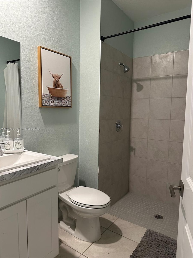 bathroom with a textured wall, tile patterned flooring, toilet, vanity, and tiled shower