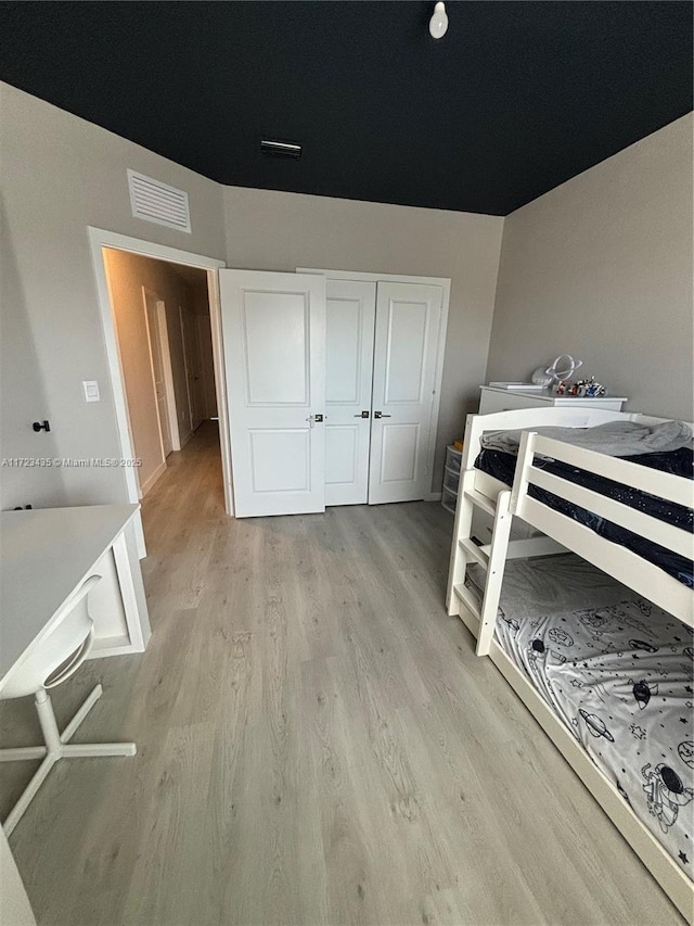 bedroom with light wood-type flooring, visible vents, and a closet