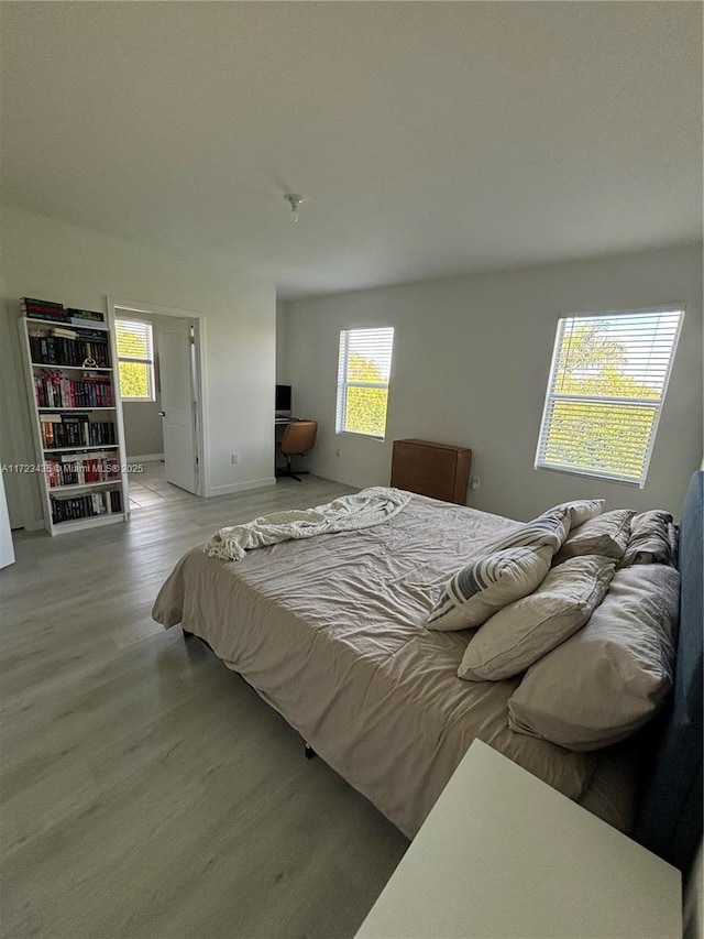 bedroom with multiple windows, wood finished floors, and baseboards