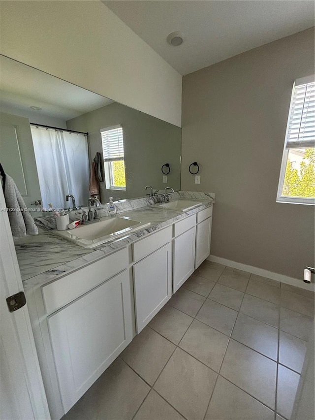 bathroom with tile patterned flooring, a sink, baseboards, and double vanity