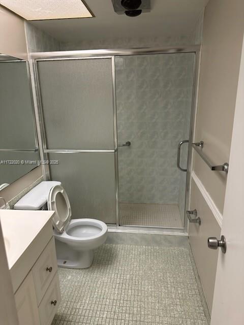 bathroom featuring tile patterned flooring, vanity, an enclosed shower, and toilet