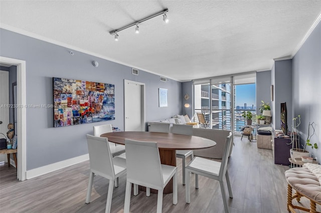 dining space featuring hardwood / wood-style flooring, expansive windows, ornamental molding, and a textured ceiling