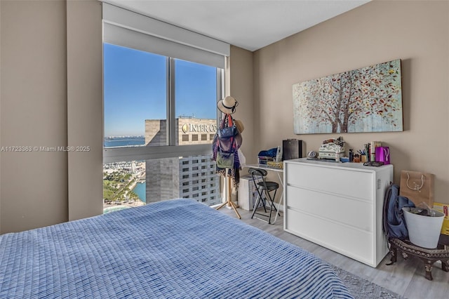 bedroom featuring a water view, light wood-type flooring, and a wall of windows