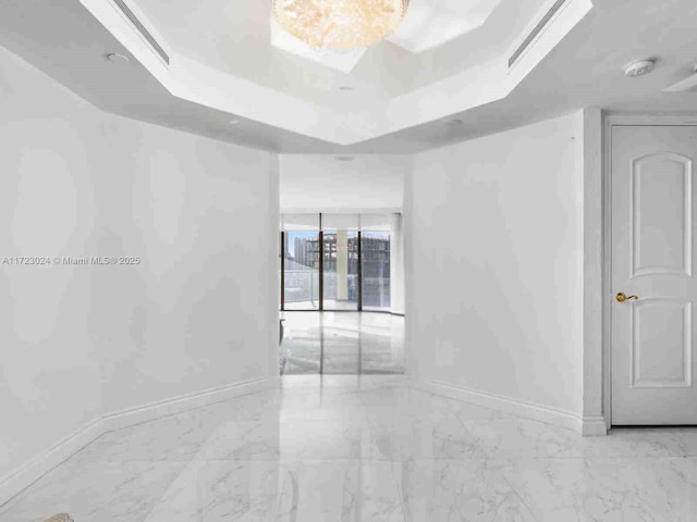 empty room featuring marble finish floor, a raised ceiling, and baseboards