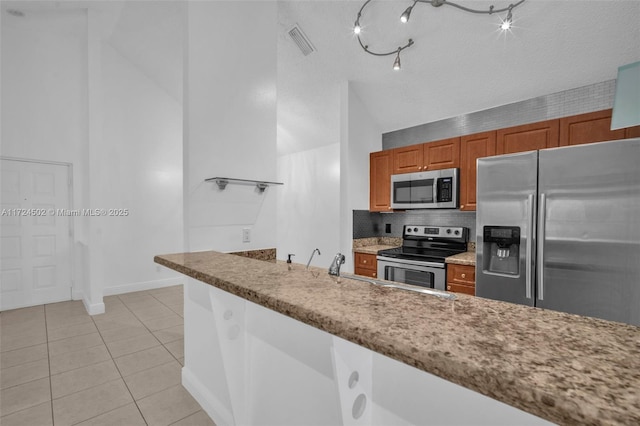 kitchen with backsplash, vaulted ceiling, a textured ceiling, light tile patterned flooring, and stainless steel appliances