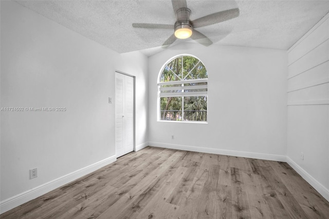 unfurnished room with a textured ceiling, ceiling fan, light hardwood / wood-style flooring, and vaulted ceiling