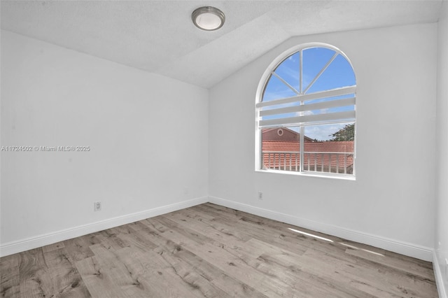 unfurnished room with a textured ceiling, light hardwood / wood-style flooring, and vaulted ceiling