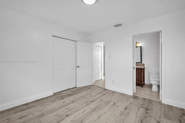 unfurnished bedroom with ensuite bath, a closet, and light wood-type flooring