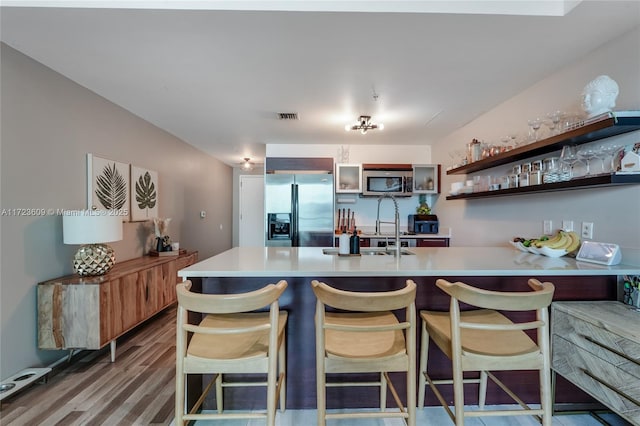 kitchen with kitchen peninsula, stainless steel appliances, sink, wood-type flooring, and a breakfast bar area