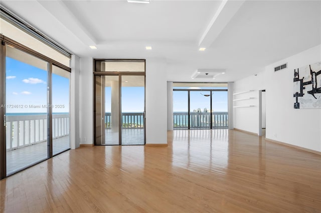 empty room featuring floor to ceiling windows, light hardwood / wood-style flooring, and a water view