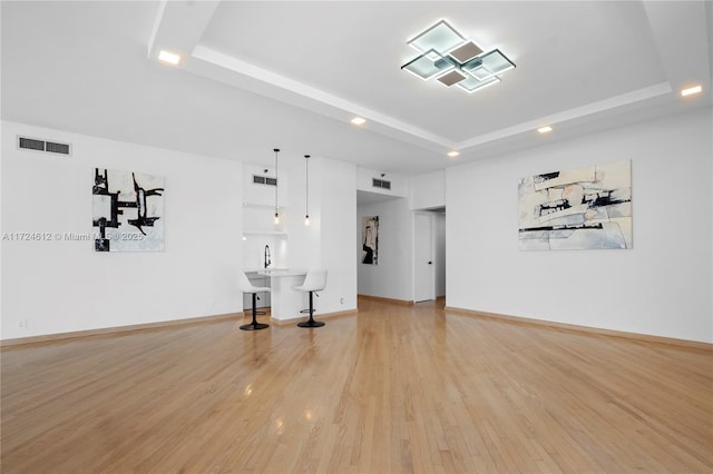 interior space with sink, light hardwood / wood-style floors, and a tray ceiling