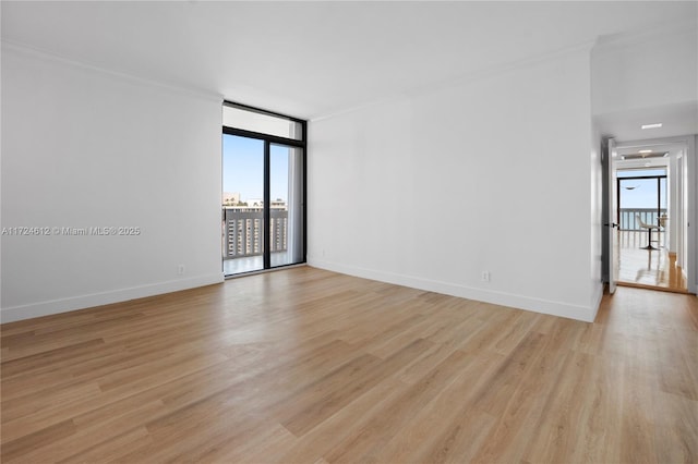 spare room featuring ornamental molding, a wall of windows, and light hardwood / wood-style flooring