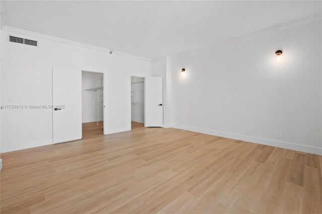 unfurnished bedroom with ornamental molding, a walk in closet, light hardwood / wood-style flooring, and a closet