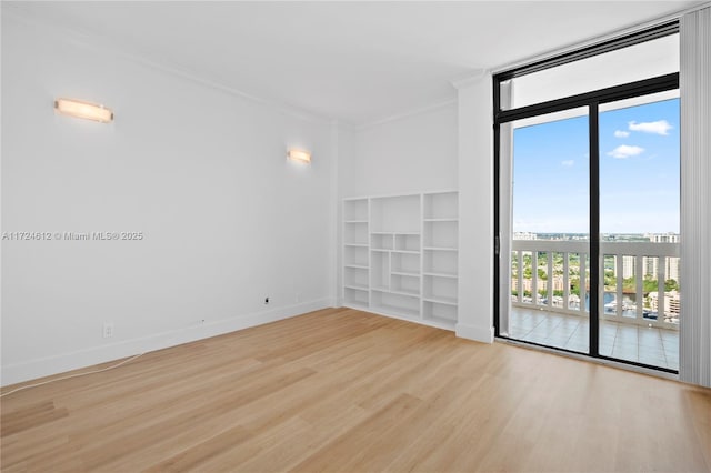 spare room with ornamental molding, built in features, a wall of windows, and light hardwood / wood-style floors