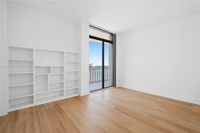 spare room featuring wood-type flooring, crown molding, and expansive windows