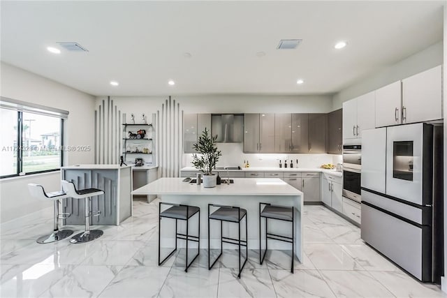 kitchen featuring gray cabinets, stainless steel appliances, an island with sink, and a kitchen bar