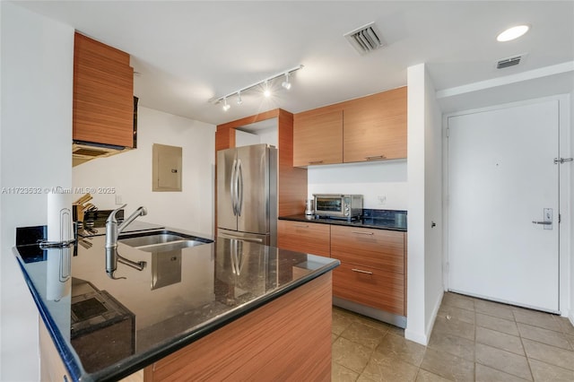 kitchen featuring kitchen peninsula, sink, dark stone countertops, electric panel, and stainless steel refrigerator