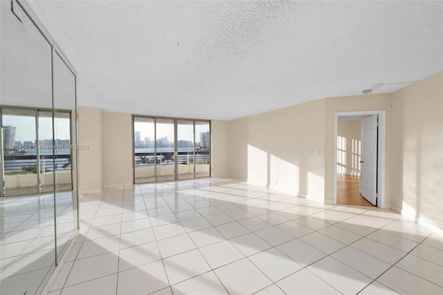 unfurnished room featuring a water view, light tile patterned floors, a textured ceiling, and floor to ceiling windows