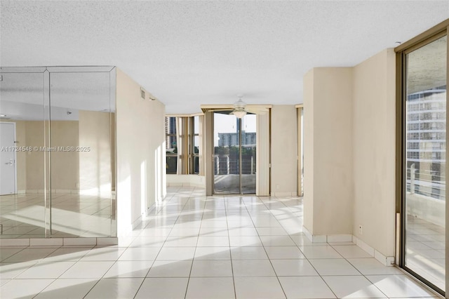 empty room featuring ceiling fan, a textured ceiling, a wall of windows, and light tile patterned flooring