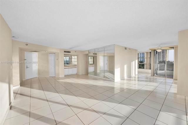 empty room with a textured ceiling, ceiling fan, and light tile patterned flooring