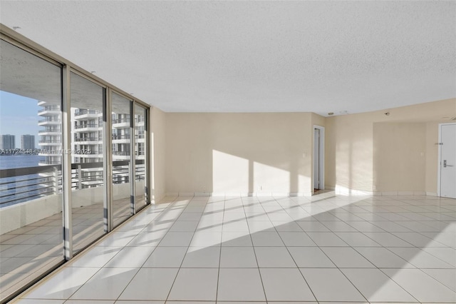 empty room with a textured ceiling, light tile patterned flooring, and expansive windows