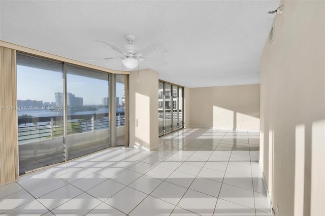 empty room with ceiling fan, a textured ceiling, light tile patterned floors, and a wall of windows