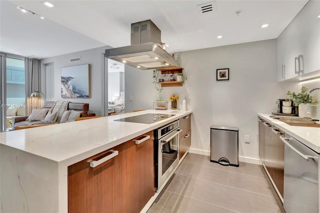 kitchen featuring sink, light tile patterned floors, stainless steel appliances, light stone countertops, and island exhaust hood