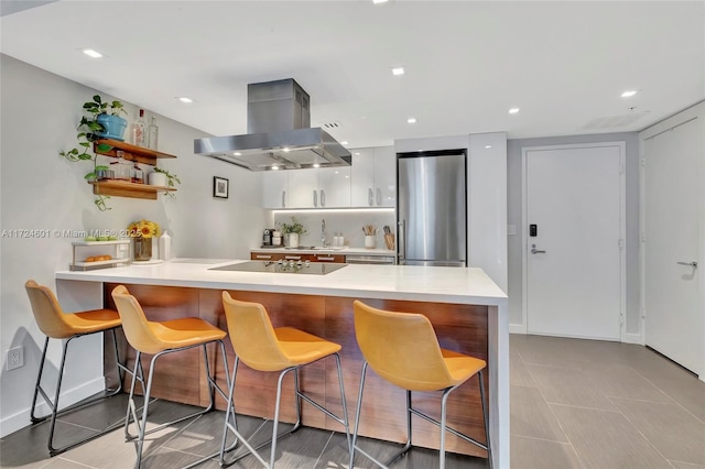 kitchen with a kitchen breakfast bar, island exhaust hood, stainless steel refrigerator, and kitchen peninsula