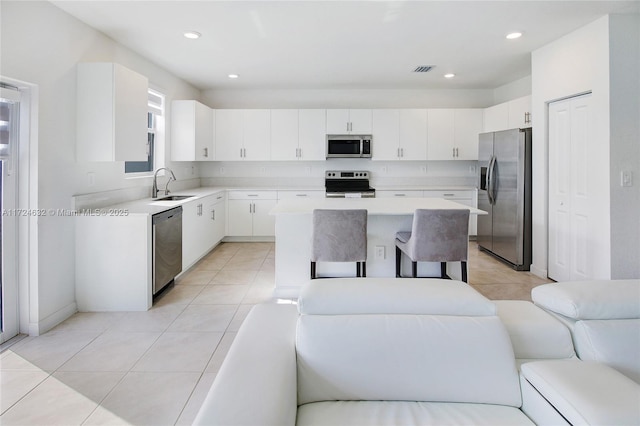 kitchen featuring light tile patterned flooring, sink, appliances with stainless steel finishes, a kitchen island, and white cabinetry