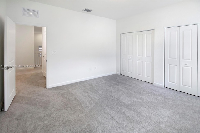 unfurnished bedroom featuring light carpet and multiple closets