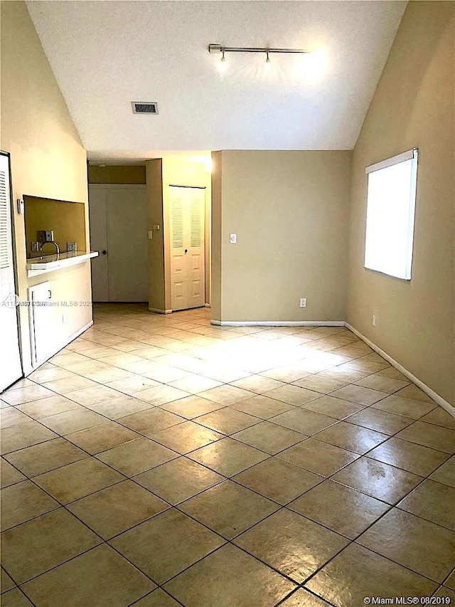 unfurnished living room featuring vaulted ceiling, light tile patterned flooring, visible vents, and a textured ceiling