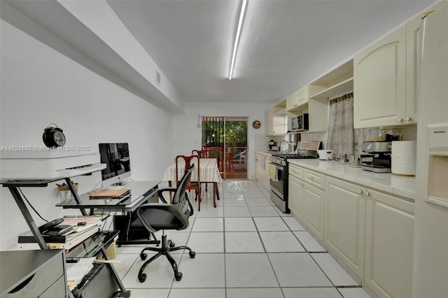 kitchen with tile countertops, backsplash, cream cabinets, light tile patterned floors, and stainless steel appliances