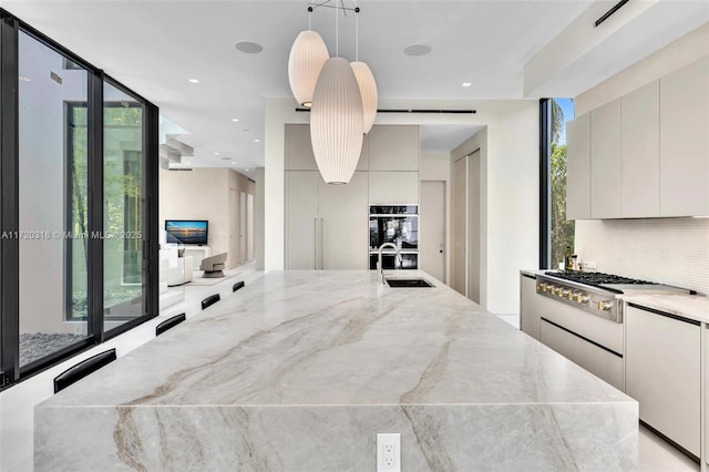 kitchen featuring light stone countertops, decorative backsplash, sink, white cabinets, and hanging light fixtures