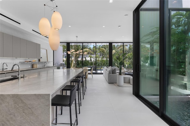 kitchen with gray cabinetry, light stone countertops, hanging light fixtures, a wall of windows, and a kitchen breakfast bar