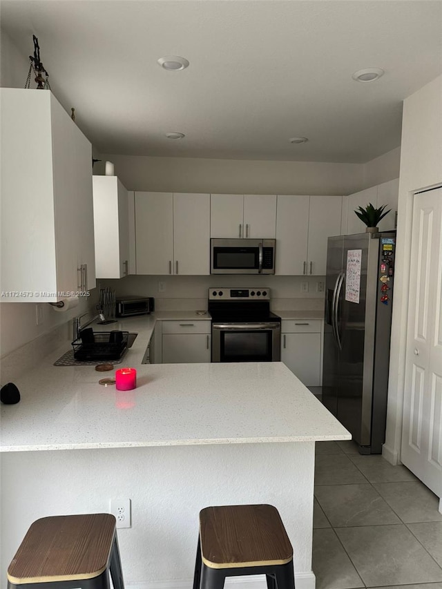 kitchen featuring a kitchen breakfast bar, kitchen peninsula, white cabinets, and appliances with stainless steel finishes